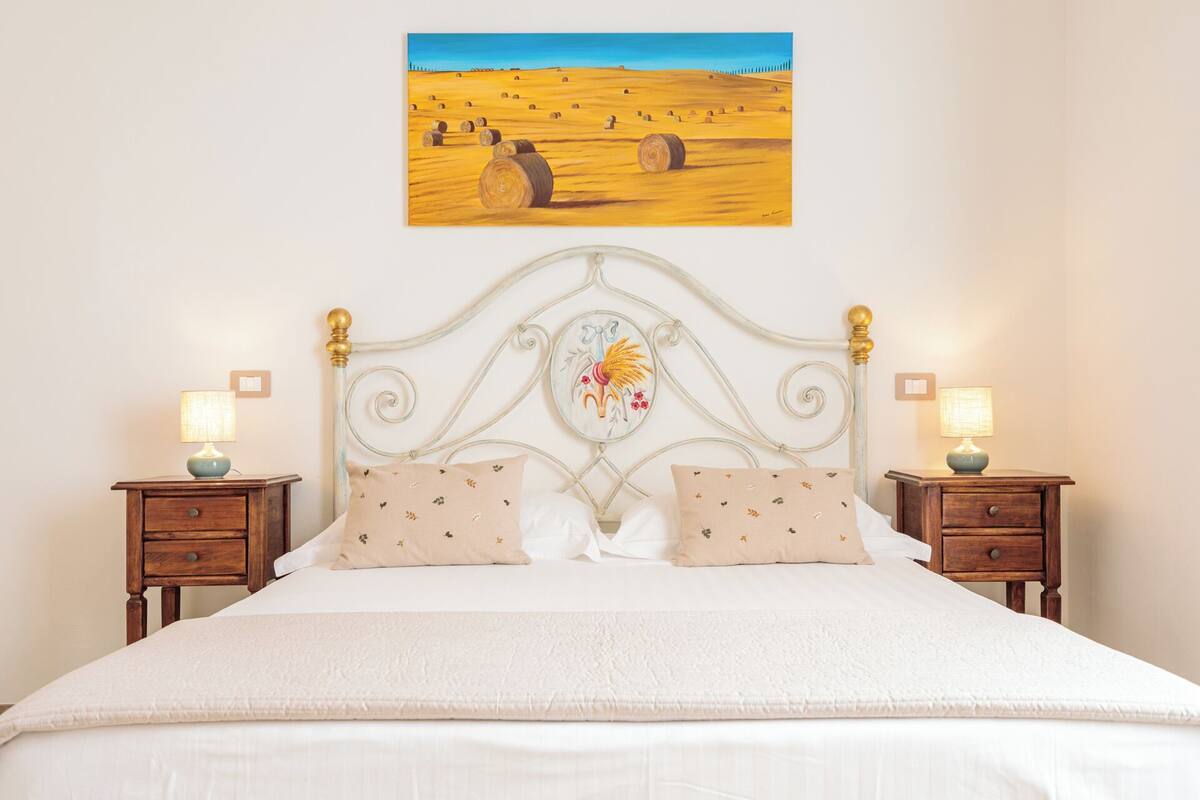 Un dormitorio con cama, dos mesitas de noche, un cuadro en la pared y un cabecero decorativo.
