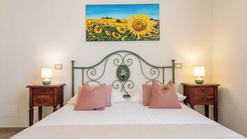 Una cama con cabecera, dos mesitas de noche y un cuadro de girasoles sobre la cama.