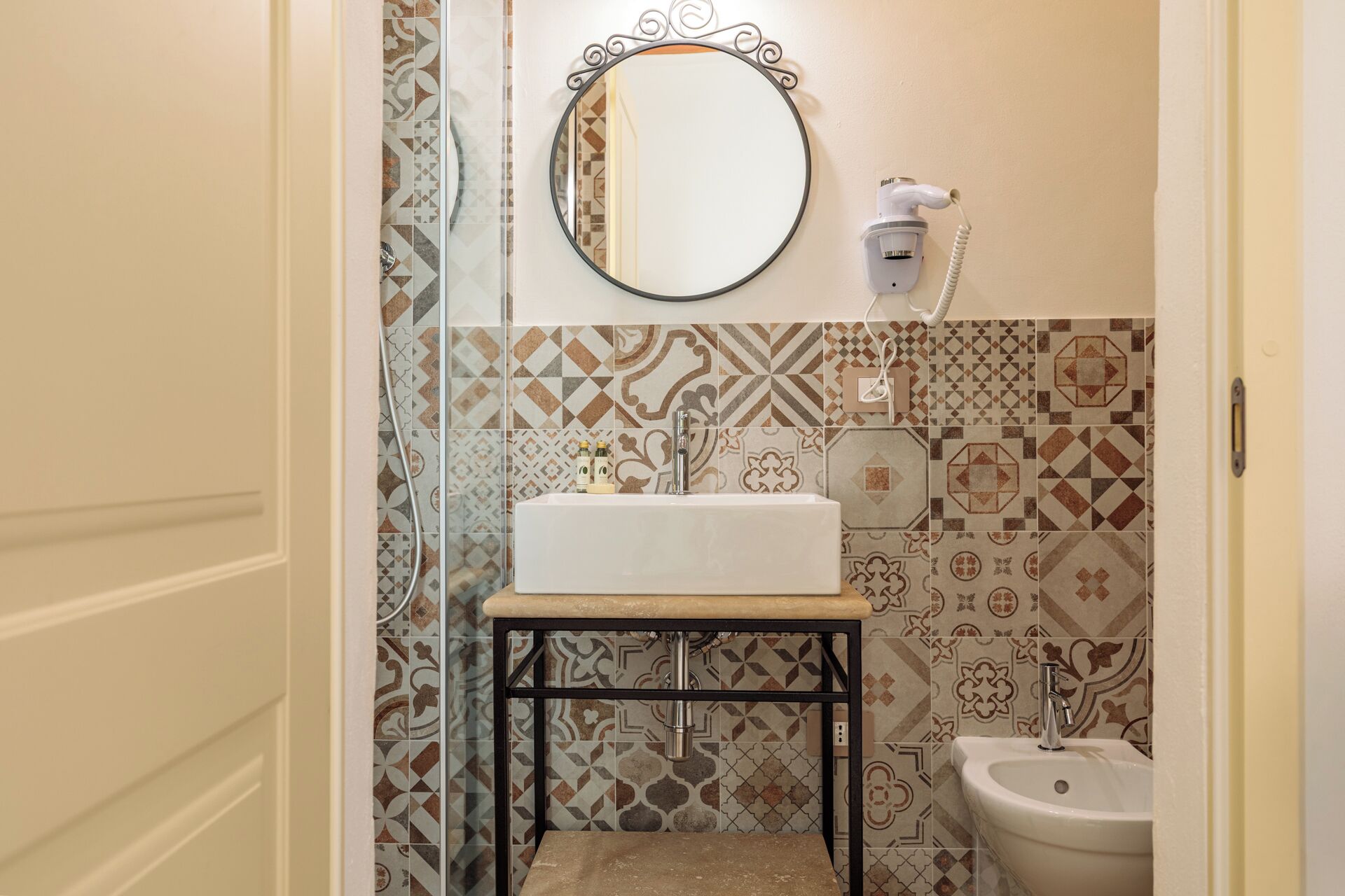 A bathroom with a white sink, a mirror, a toilet, and patterned tiles.