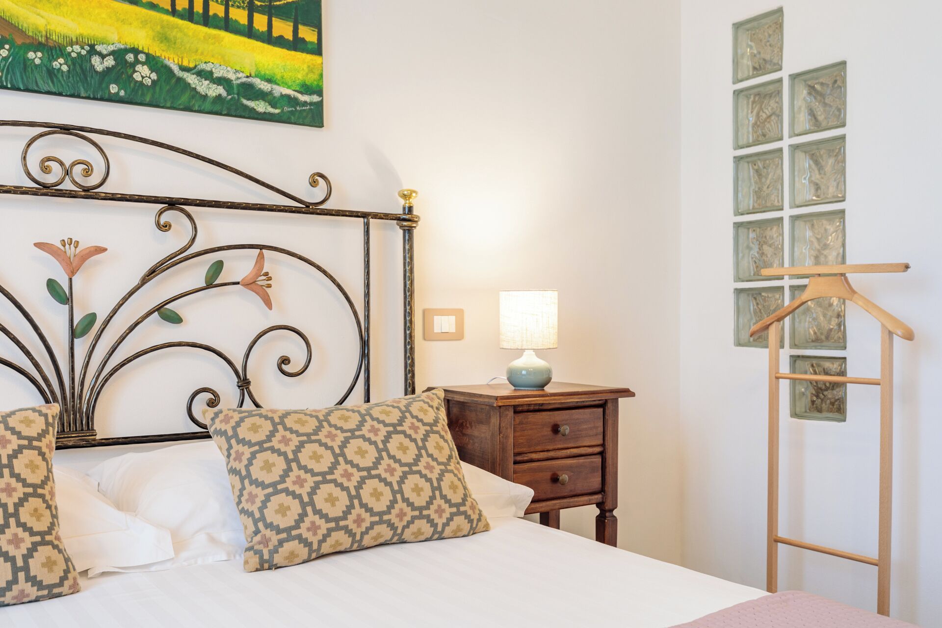 A neatly made bed with patterned pillows, a bedside table with a lamp, and a wooden hanger on a wall.