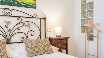 A neatly made bed with patterned pillows, a bedside table with a lamp, and a wooden hanger on a wall.