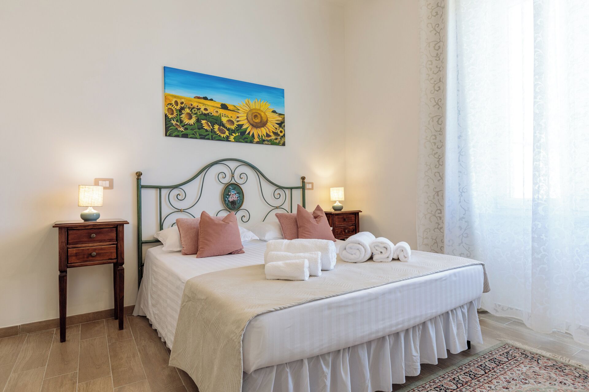 A neatly made bed with pillows, a bedside lamp, and a painting of sunflowers on the wall.