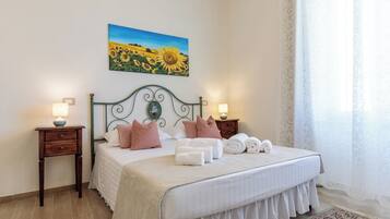 A neatly made bed with pillows, a bedside lamp, and a painting of sunflowers on the wall.