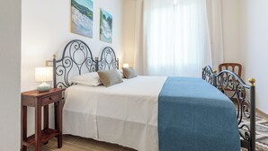 Une chambre à coucher comprenant un lit, une table de chevet, une lampe, une fenêtre avec des rideaux et deux tableaux accrochés au mur.