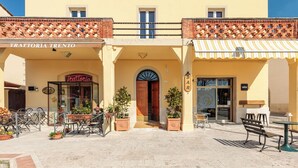 Un bâtiment sur lequel on peut lire l’inscription « TRATTORIA TRENTO » et une autre inscription indiquant « BAR ». Il y a des espaces extérieurs aménagés avec des tables et des chaises.