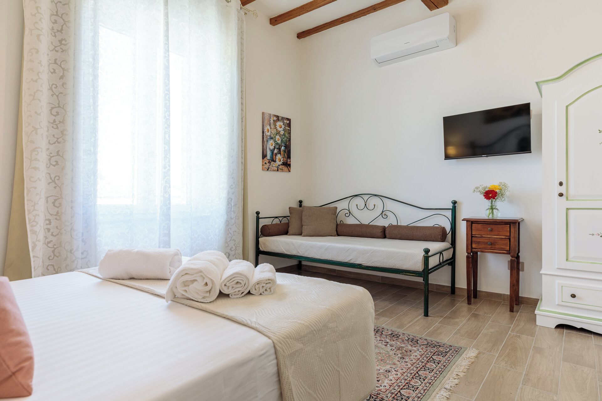 A bedroom with a bed, a sofa, a TV, a small table, and a wardrobe.