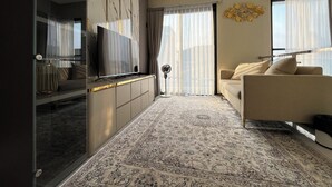 A modern living room with a flat-screen TV, a sofa, a patterned rug, and a large window with sheer curtains. - Arrayyan Executive Village Complex Batu (Batu)