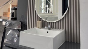 A modern bathroom with a white sink, a round mirror, and a striped wall. - Arrayyan Executive Village Complex Batu (Batu)
