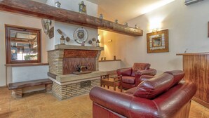A living room with a fireplace, leather sofa, wooden bench, and a stone-tiled floor. - Tenuta dell'Argento - Room 7 by Rentbeat (Civitavecchia)