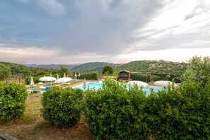 A pool area with umbrellas, a wooden deck, and a view of hills. - Tenuta dell'Argento - Room 7 by Rentbeat (Civitavecchia)