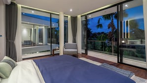 A modern bedroom with a large bed, a chair, and a view of a balcony with glass doors. - Villa Fortuna by RPM (Kerobokan)