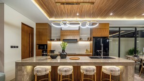 A modern kitchen with a central island, bar stools, wooden cabinets, and a built-in stove. - Villa Fortuna by RPM (Kerobokan)