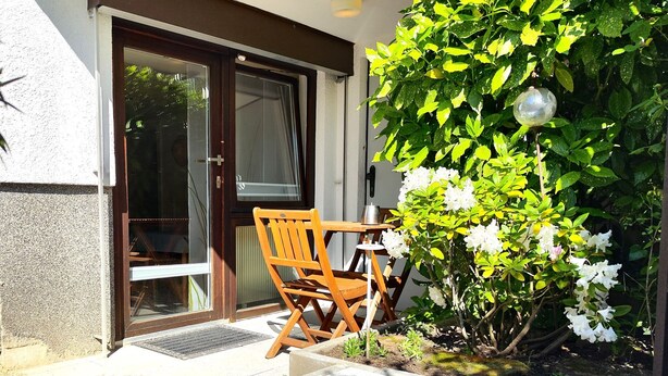 Une chaise et une table en bois se trouvent devant un bâtiment doté d’une porte et d’une fenêtre.