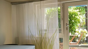 Une pièce avec une table, des chaises, une porte donnant sur l’extérieur et une grande plante dans un coin.
