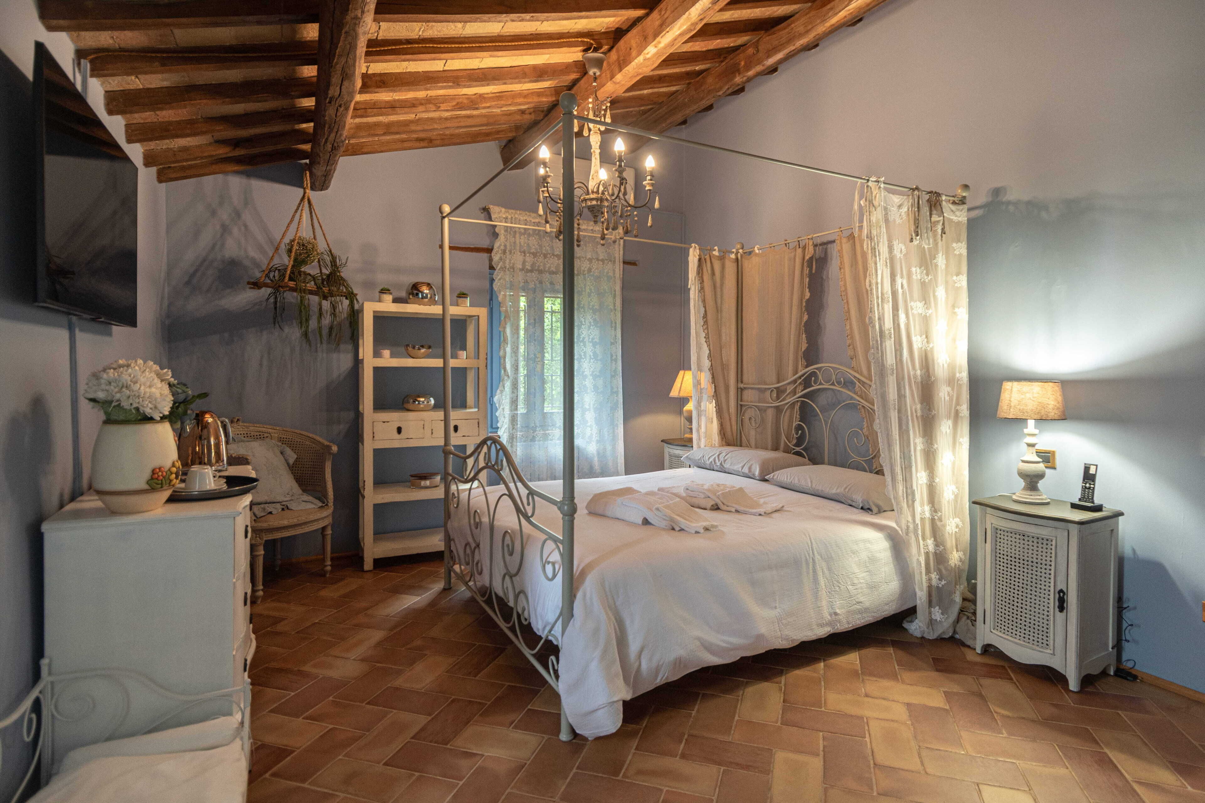 Un letto a baldacchino con tenda, un comodino con lampada, una sedia, un piccolo armadio e un televisore a parete.