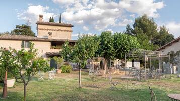 Un patio con una pérgola, mobiliario exterior y un edificio con techo de tejas.