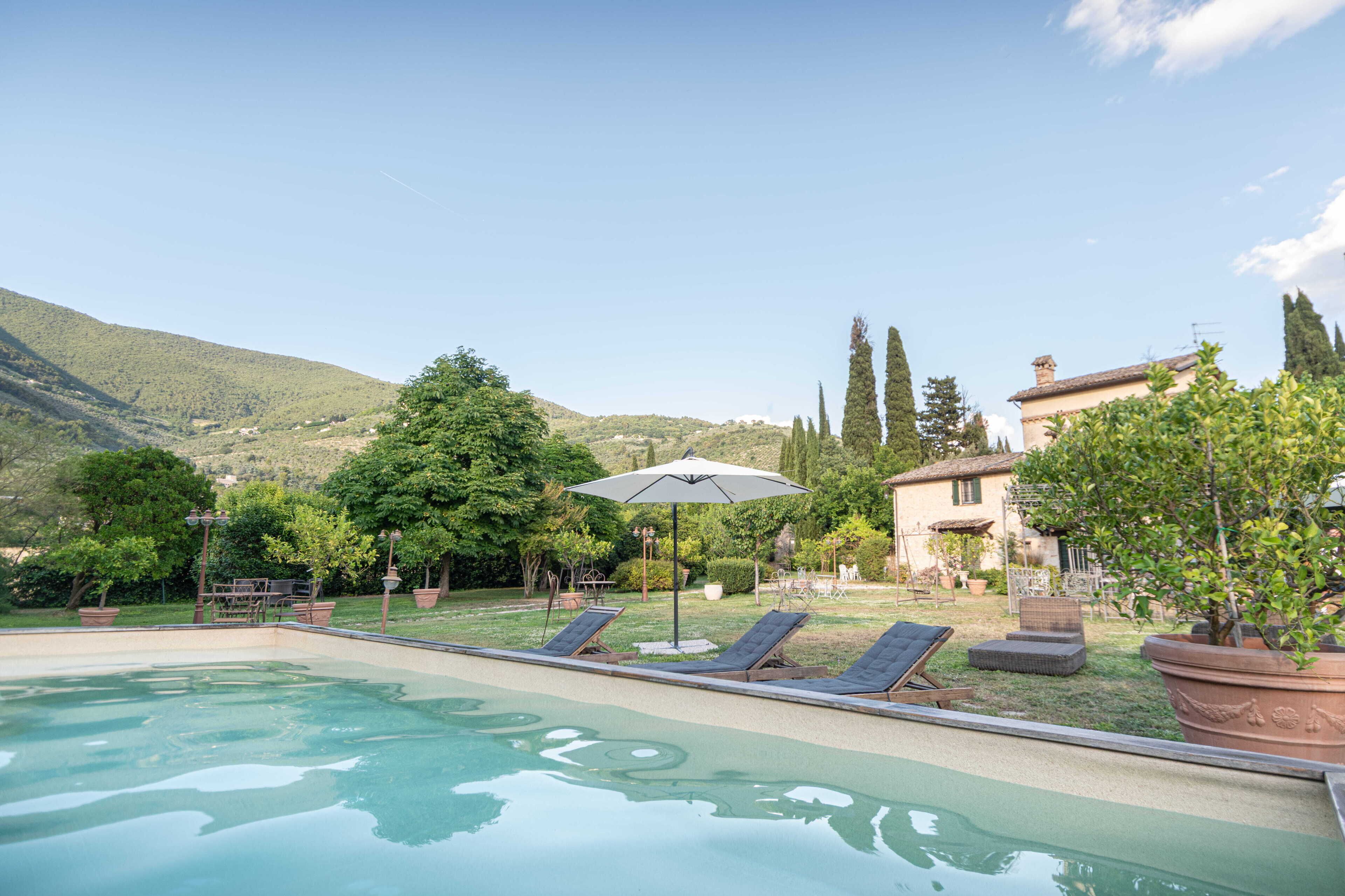 Una piscina con lettini e ombrellone, circondata da vegetazione e da un pendio.