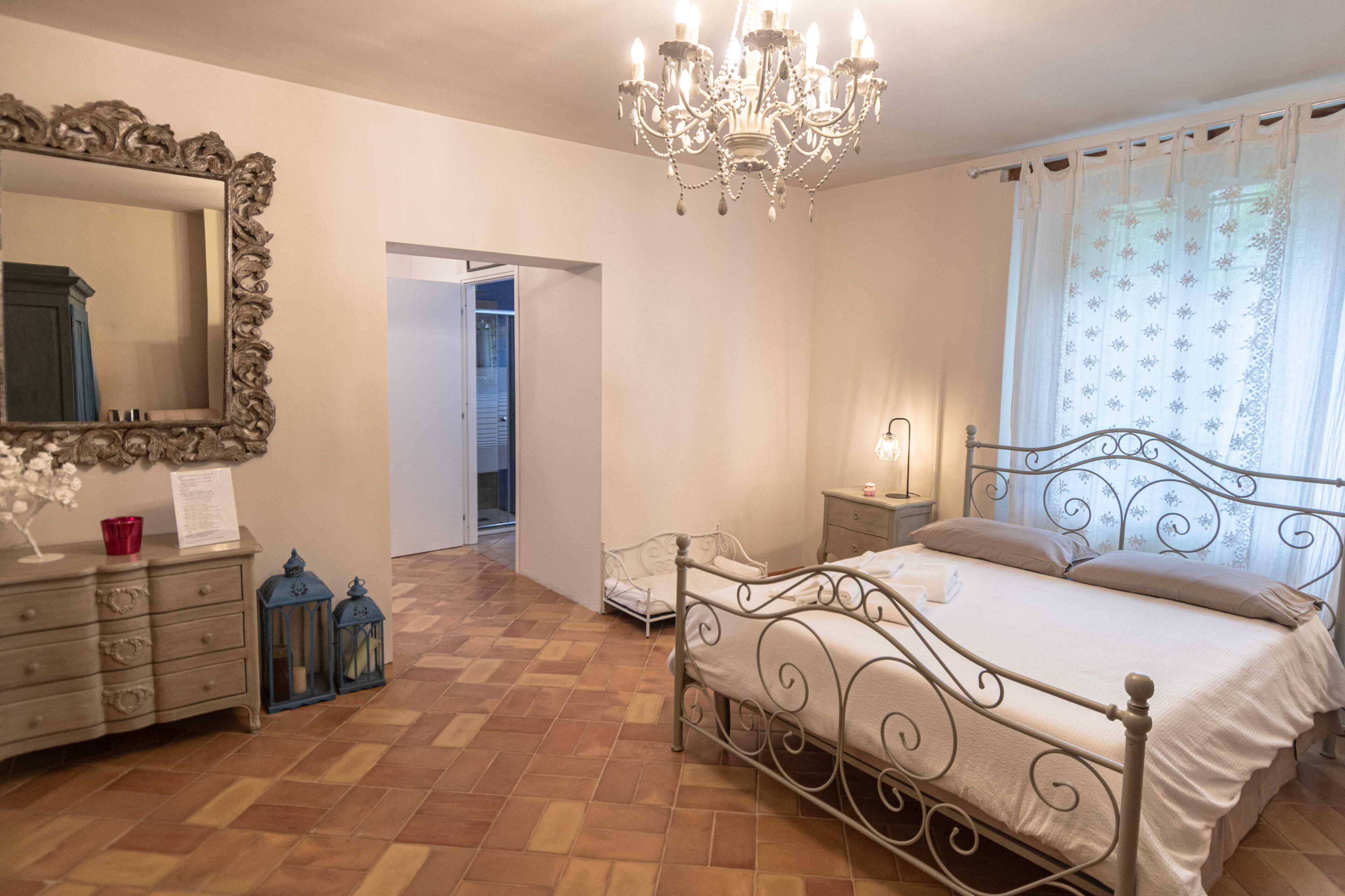 Un dormitorio con cama, cómoda, espejo, candelabro y una puerta que da a otra habitación.