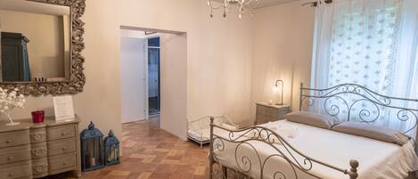 Un dormitorio con cama, cómoda, espejo, candelabro y una puerta que da a otra habitación.