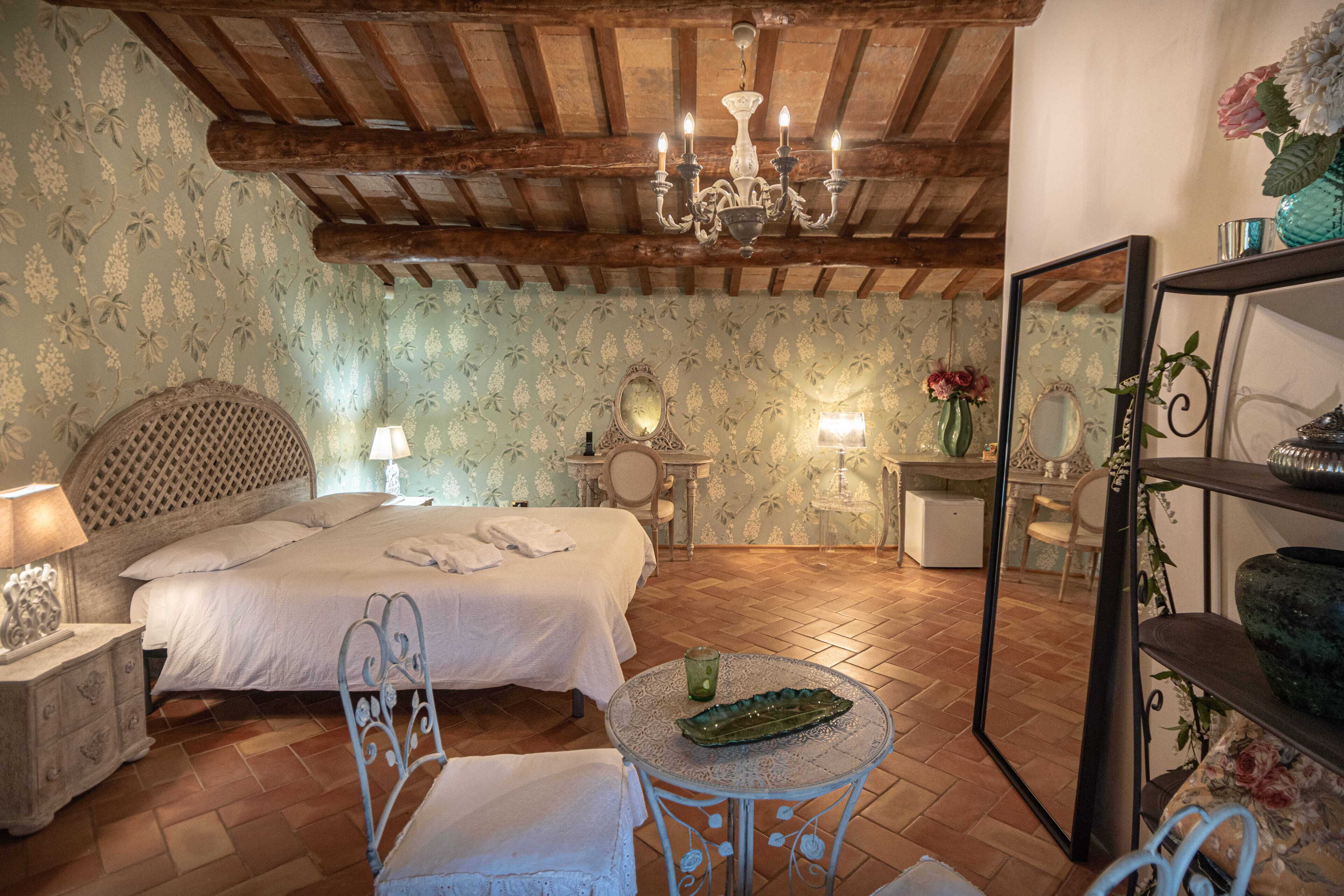 Un dormitorio con cama, mesita de noche, lámpara, espejo y una mesa redonda con un objeto decorativo.