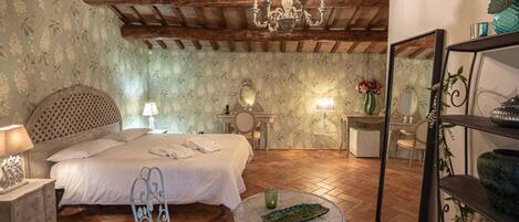 Un dormitorio con cama, mesita de noche, lámpara, espejo y una mesa redonda con un objeto decorativo.
