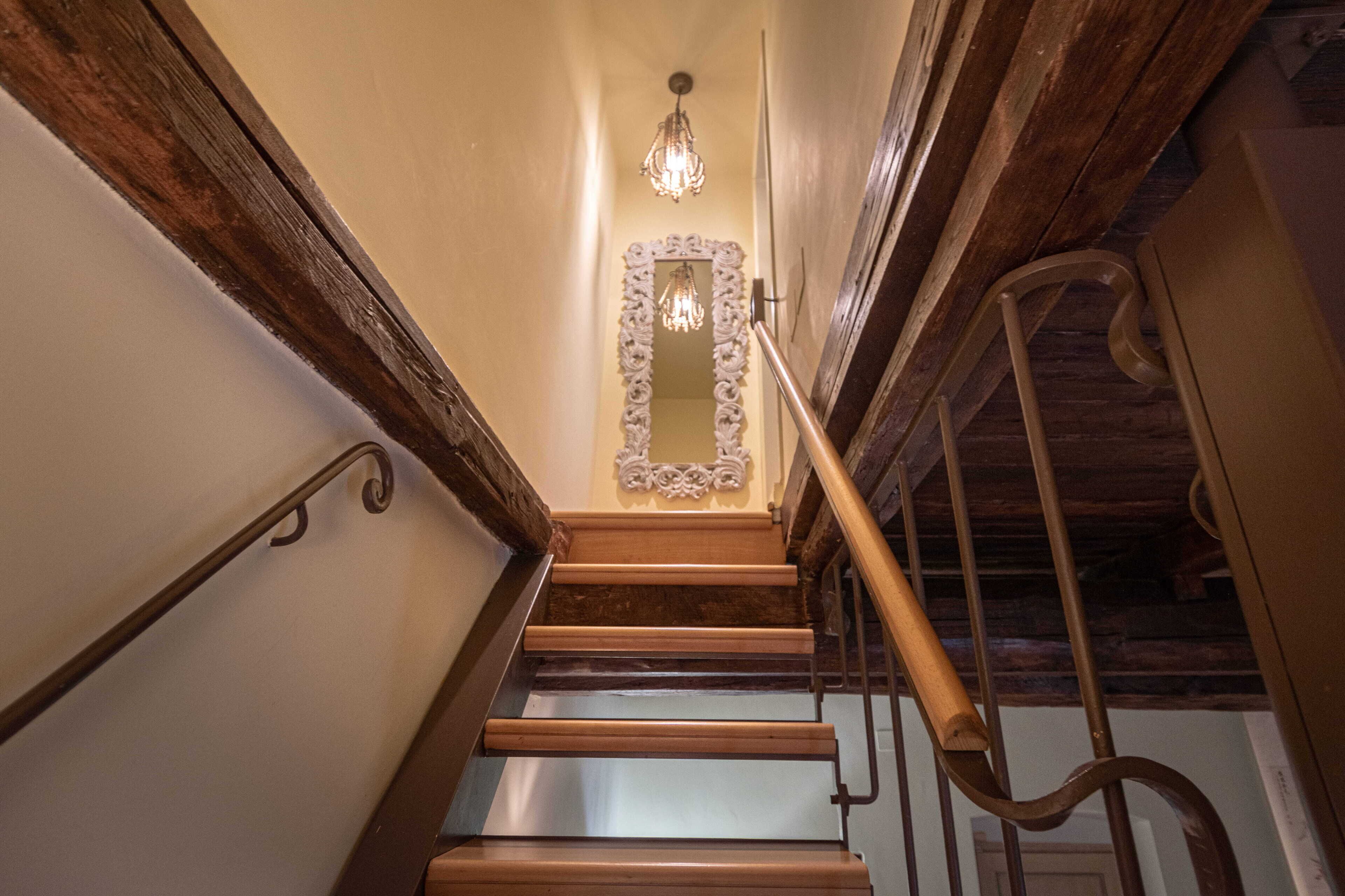 Una escalera de madera con barandilla de metal, un candelabro y un espejo decorativo en la pared.