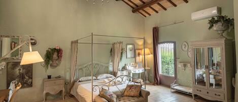 A four-poster bed with a canopy, a bedside table with a lamp, a dresser with a mirror, and a window with curtains.