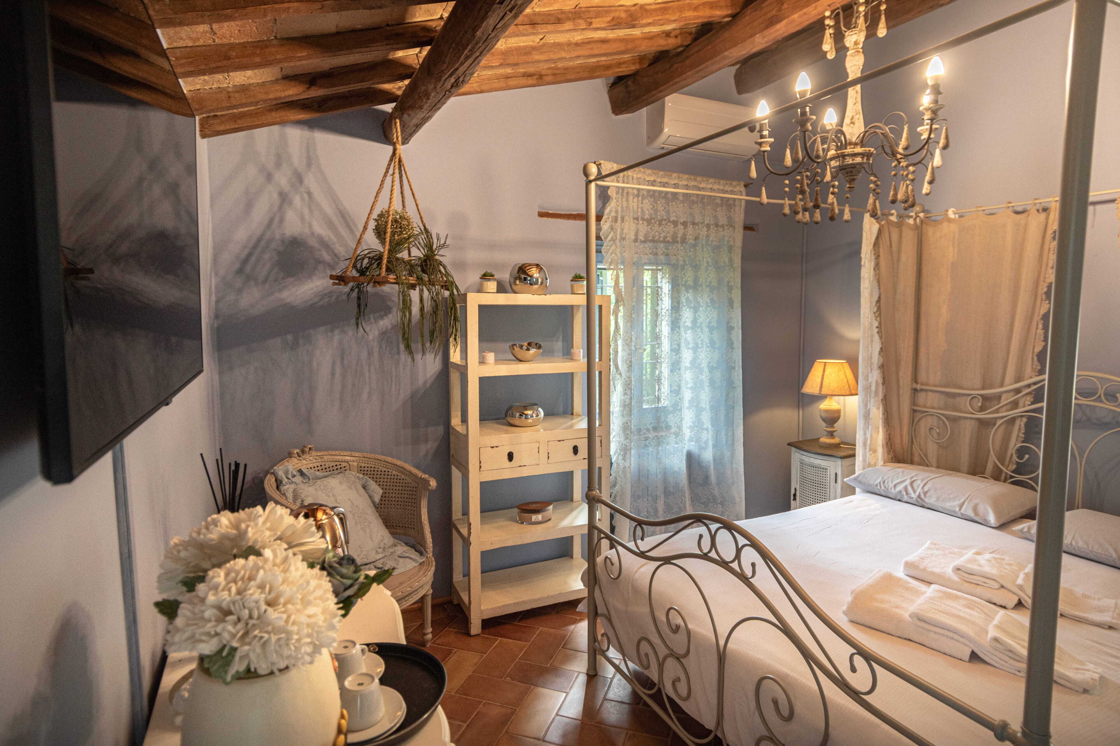 Un lit à baldaquin, une table de chevet avec une lampe, une plante suspendue et une étagère blanche.