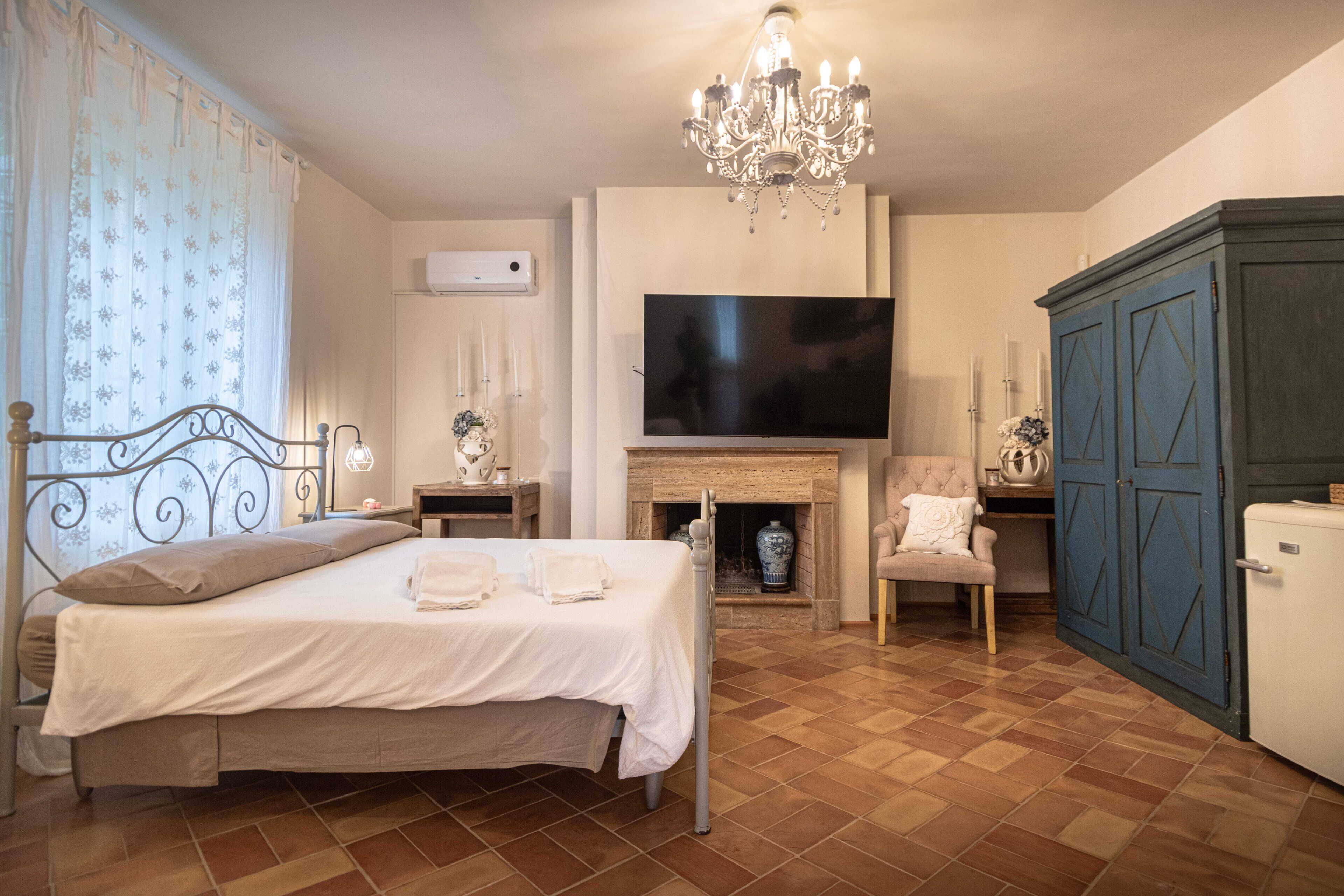 Een slaapkamer met een bed, een televisie, een open haard, een kledingkast en een kroonluchter.