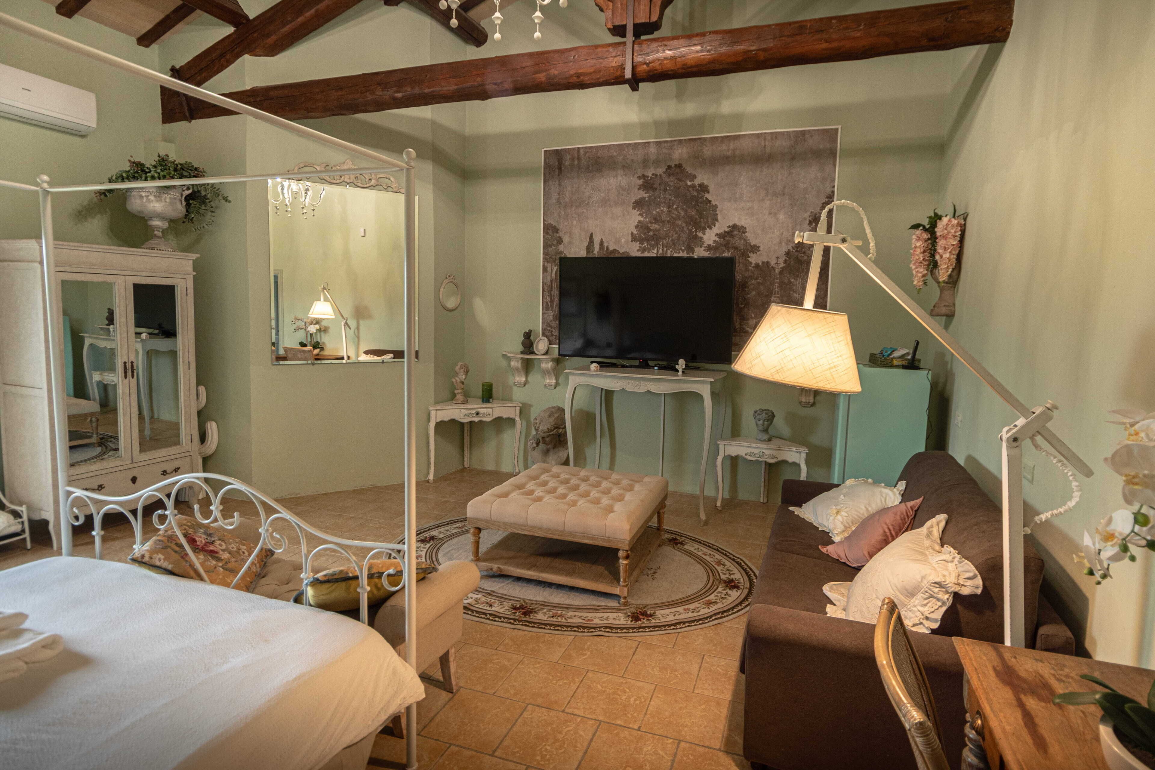A bedroom with a four-poster bed, a television, a desk, and a chair.
