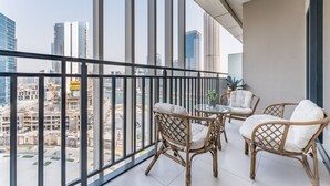 Een balkon met rieten stoelen en een tafeltje, met uitzicht op een stadsgezicht met hoge gebouwen en bouwplaatsen.