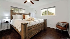 Una camera da letto con un letto di legno, una ventola a soffitto, un comodino, una sedia e una finestra.