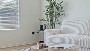 A modern living room with a white sofa, a round wooden coffee table, a small wooden side table, a floor lamp, and a potted plant. - Don't Miss Where the Fun Is 4BR/3BA Home Near DT! (San Antonio)