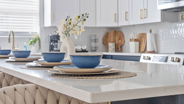 A modern kitchen with white cabinets, a marble countertop, and blue bowls on a placemat. - Don't Miss Where the Fun Is 4BR/3BA Home Near DT! (San Antonio)