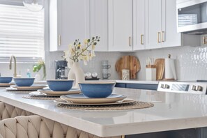 Een moderne keuken met witte kasten, een marmeren aanrechtblad en blauwe kommen op een placemat.