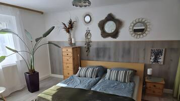 Une chambre à coucher comprenant un lit, une commode, une plante en pot, des décorations murales et une table de chevet.
