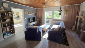 Un salon avec un canapé, une table basse, une bibliothèque, un téléviseur et une fenêtre avec des rideaux.