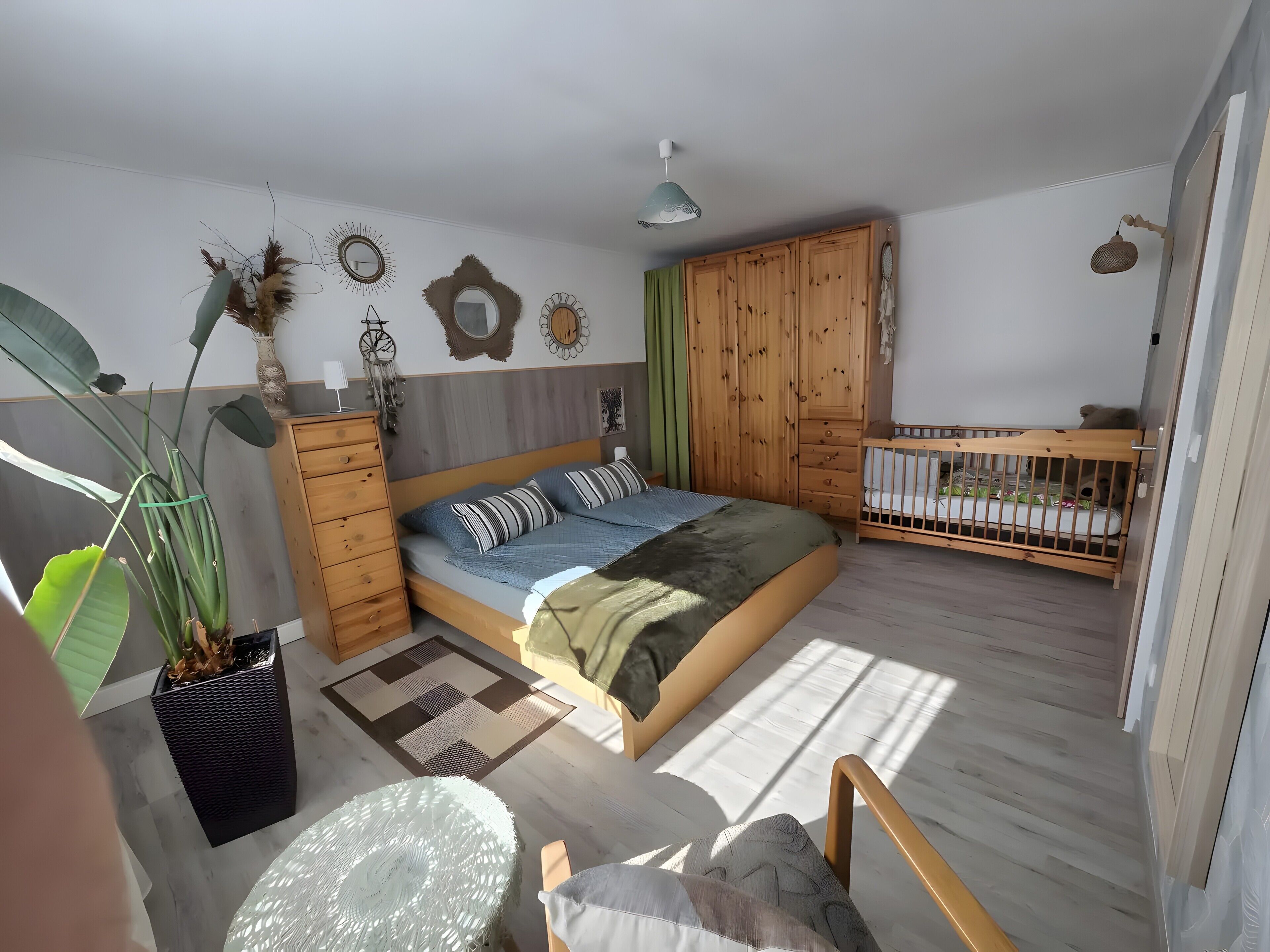 Un dormitorio con una cama, una cuna, un aparador y una planta grande.
