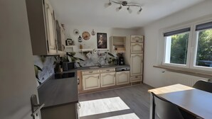 Une cuisine avec un coin repas, des meubles de rangement en bois, une fenêtre avec des stores et un radiateur.
