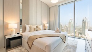 Une chambre d’hôtel moderne avec un grand lit, deux tables de chevet, une petite table et une vue sur le paysage urbain.