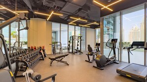 Une salle de sport moderne, dotée de divers appareils d’entraînement, de grandes fenêtres et offrant une vue sur le paysage urbain.