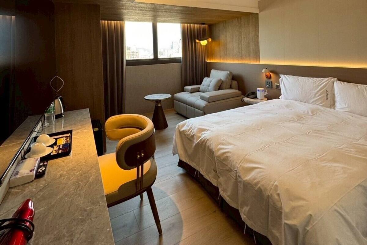 Una habitación de hotel moderna con una cama grande, un sofá, un escritorio con una silla y una mesita.