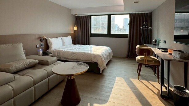 A modern hotel room with a bed, sofa, dining table, and a view of the city. - Fooyee Hotel - Yizhong Branch (Taichung)