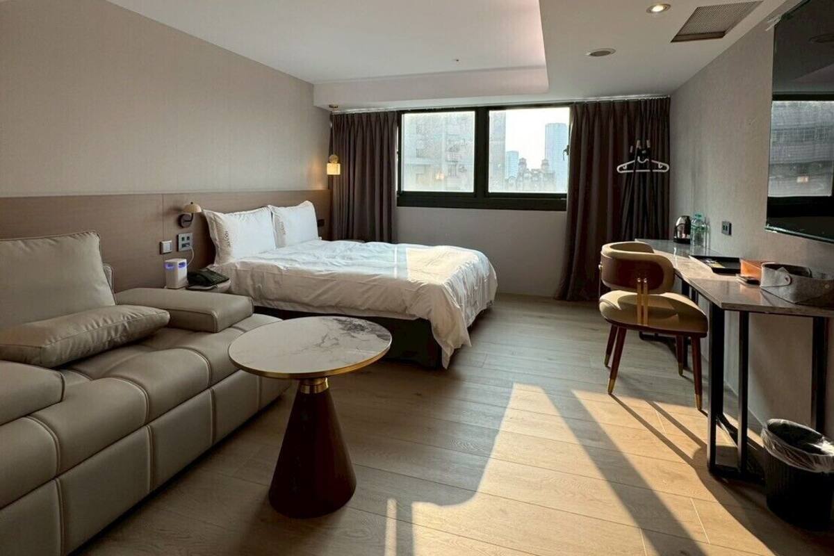 Una habitación de hotel moderna con cama, sofá, mesa de comedor y vistas a la ciudad.