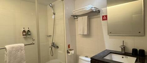 Un baño moderno con ducha de vidrio, inodoro y lavamanos con espejo.