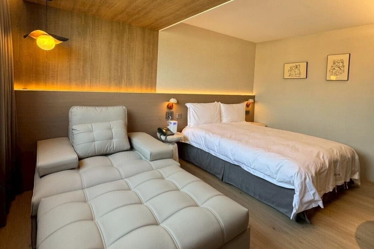 Un dormitorio moderno con sofá cama, una cama individual y una mesita de noche con lámpara.