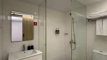 A modern bathroom with a glass-enclosed shower, a white sink with a mirror above it, and a toilet.