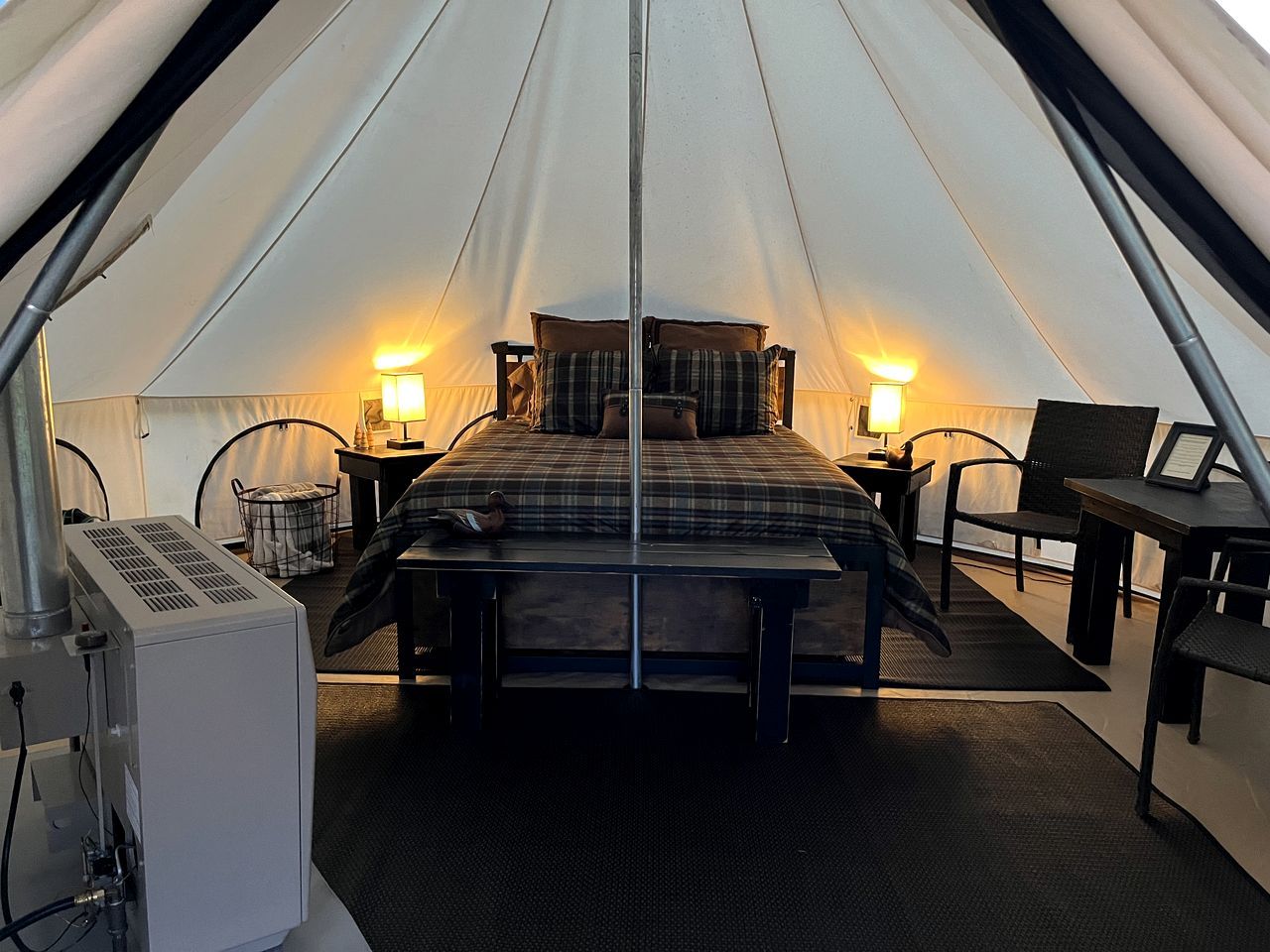 A tent with a bed, two bedside tables, a chair, and a table.