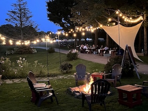 Un espace extérieur aménagé avec des chaises, des tables, un foyer et des guirlandes lumineuses.