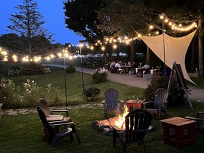 Un espace extérieur aménagé avec des chaises, des tables, un foyer et des guirlandes lumineuses.